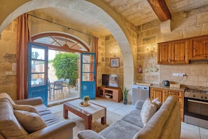 A cozy living room with a sofa, a coffee table, and a TV. There's a stone wall and wooden beams.