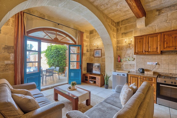 A cozy living room with a sofa, a coffee table, and a TV. There's a stone wall and wooden beams. - Xaghra 5BDR Farmhouse with Pool by PMI Malta (Ix-Xagħra)