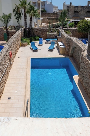 Una piscina con agua azul, rodeada de muros de piedra y palmeras.