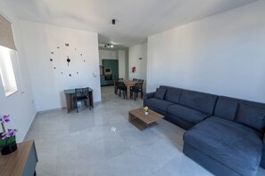 Ein modernes Wohnzimmer mit grauem Sofa, einem Holztisch, einem Esstisch mit Stühlen und einer Wanduhr.