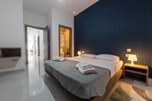 A modern hotel room with a large bed, bedside lamps, a wooden nightstand, and a view of a hallway. - Swieqi 3BDR New Apartment 12 (Is-Swieqi)