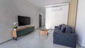 Ein modernes Wohnzimmer mit Flachbildfernseher, einem Holzkonsolentisch, einem grauen Sofa und einem Couchtisch.