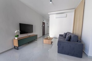 Ein modernes Wohnzimmer mit Flachbildfernseher, einem Holzkonsolentisch, einem grauen Sofa und einem Couchtisch.