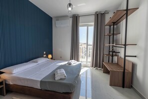 Ein modernes Hotelzimmer mit einem großen Bett, einer Holzbank, einem Balkon mit Aussicht und einer Klimaanlage.
