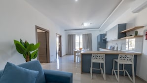 A modern living room with a blue sofa, a kitchen with a bar area, and a dining space. - Swieqi Brand New 3BDR Flat- Spacious Getaway - FL7 (Is-Swieqi)