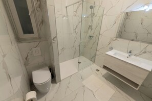 Uma casa de banho com cabine de chuveiro em vidro, sanita e lavatório com espelho em cima.