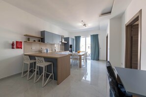 Uma cozinha moderna com uma ilha central, banquetas brancas, uma mesa de jantar com cadeiras e vista para o exterior através de grandes janelas.