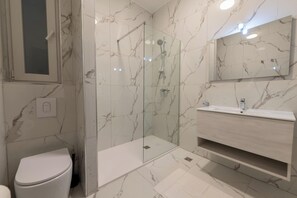 Une salle de bain moderne avec une douche en verre, des toilettes blanches et un mur recouvert de carreaux de marbre.
