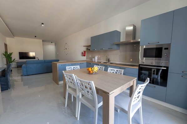 A modern kitchen with blue cabinets, a built-in oven, and a dining area with white chairs.