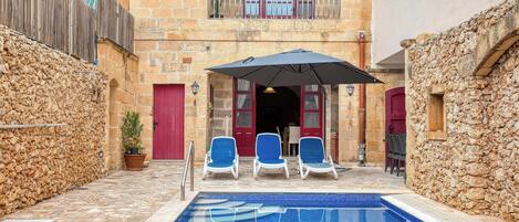 A pool area with blue tiled flooring, a red door, and a balcony with a railing.