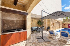 An outdoor patio with a barbecue grill, dining table, chairs, and a pool area. - Tan Nanna 5 BDR Farmhouse by PMI Malta (Ix-Xagħra)