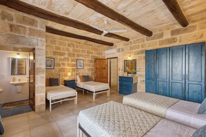 A room with stone walls, wooden beams, a ceiling fan, a bed with a patterned bedspread, a dresser, and a wardrobe. - Tan Nanna 5 BDR Farmhouse by PMI Malta (Ix-Xagħra)