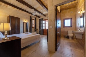 Ein Schlafzimmer mit Bett, Nachttisch und einem Badezimmer inklusive Toilette und Waschbecken.