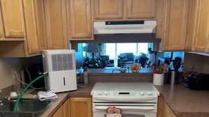 A compact kitchen with wooden cabinets, a white stove, a dishwasher, and a window providing natural light. -  2-bedroom condo in charming Cape Canaveral with amazing ocean views (Cape Canaveral)