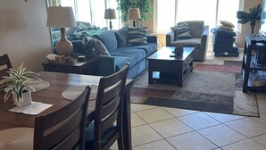 A living room with a sofa, coffee table, dining table, chairs, and a TV. -  2-bedroom condo in charming Cape Canaveral with amazing ocean views (Cape Canaveral)