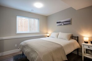 Een slaapkamer met een bed, een raam, een nachtkastje en een aan de muur hangend schilderij.