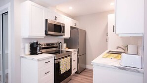 A compact kitchen with white cabinets, a microwave, a refrigerator, an oven, and a sink.