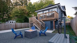A backyard with a fire pit, two blue chairs, a wooden deck, and a staircase leading to a decked area.