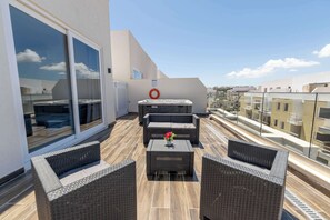Eine Dachterrasse mit Korbmöbeln, einem Whirlpool und einem Glasgeländer mit Blick auf die Stadt.