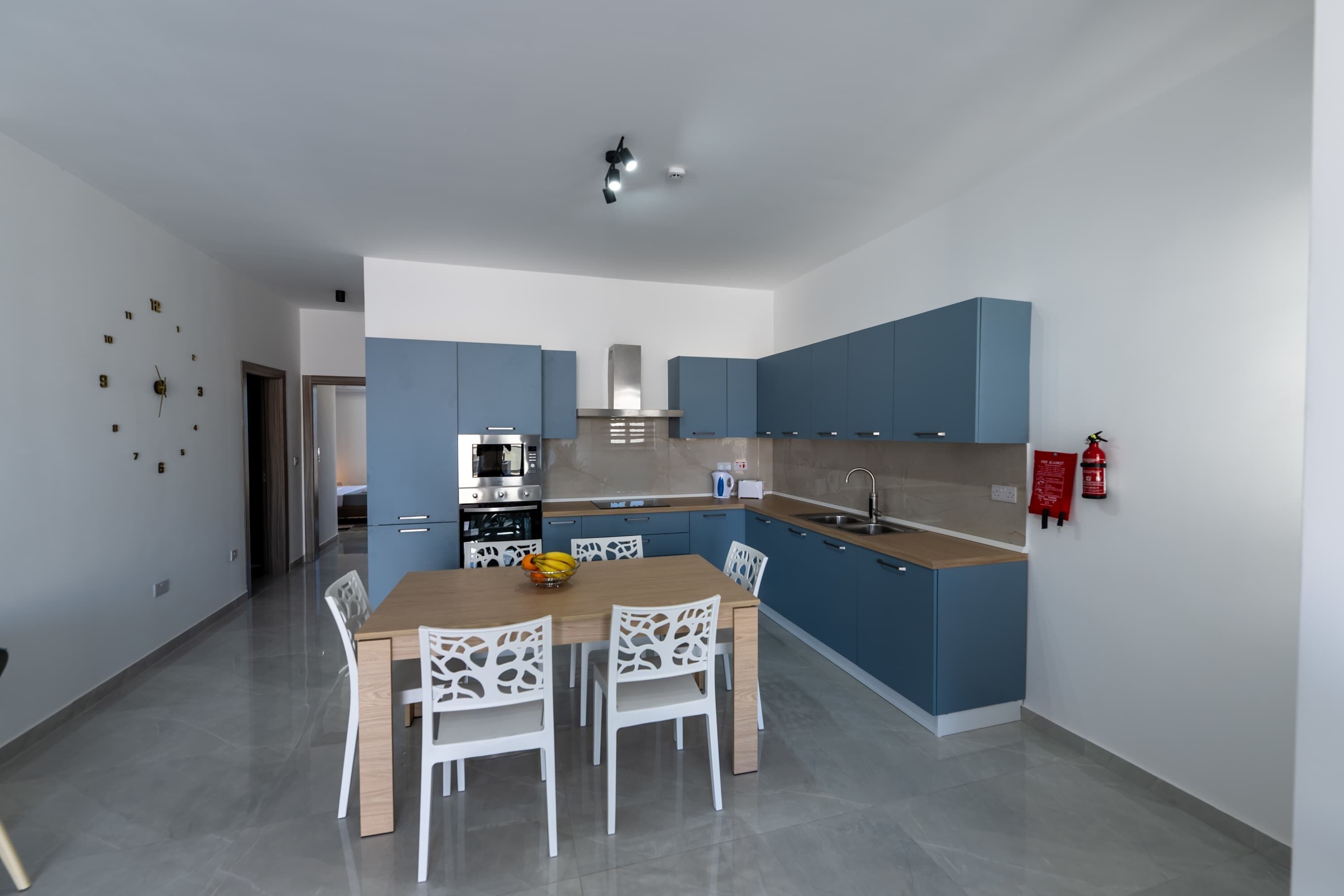 Une cuisine moderne avec des meubles bleus, une table à manger en bois et des chaises blanches.