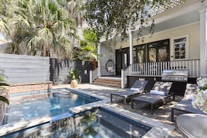 Ein Garten mit Swimmingpool, Liegestühlen, Grill und einer überdachten Terrasse.