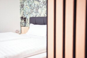 A hotel room with a bed, a nightstand, a lamp, and a floral wallpaper. - Central Kempten | Sleeps 2 • Stylish (Kempten (Allgäu))