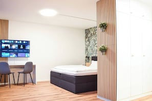 Quarto moderno com cama, escrivaninha e duas cadeiras, TV de tela plana e guarda-roupa.