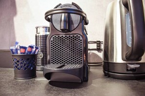 Eine Kaffeemaschine, ein Wasserkocher und eine Tasse mit Kaffeekapseln auf einer Arbeitsplatte.