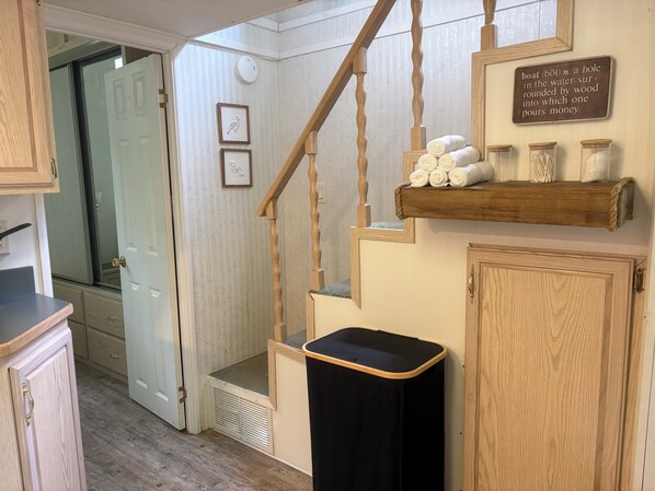 A staircase with wooden railings, a black trash bin, a shelf with rolled towels, and a wall-mounted sign.