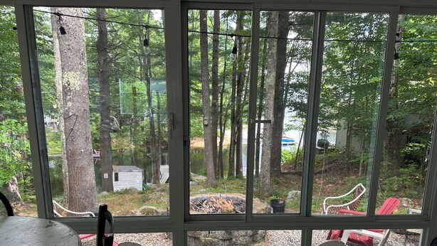 Huone, jossa on suuri ikkuna, josta avautuu näkymä metsäiselle alueelle, ulkotila, jossa on Adirondack-tyylisiä tuoleja, sekä pieni nuotiopaikka.