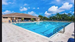 Una piscina con lettini, un edificio con tetto in tegole e palme sullo sfondo.
