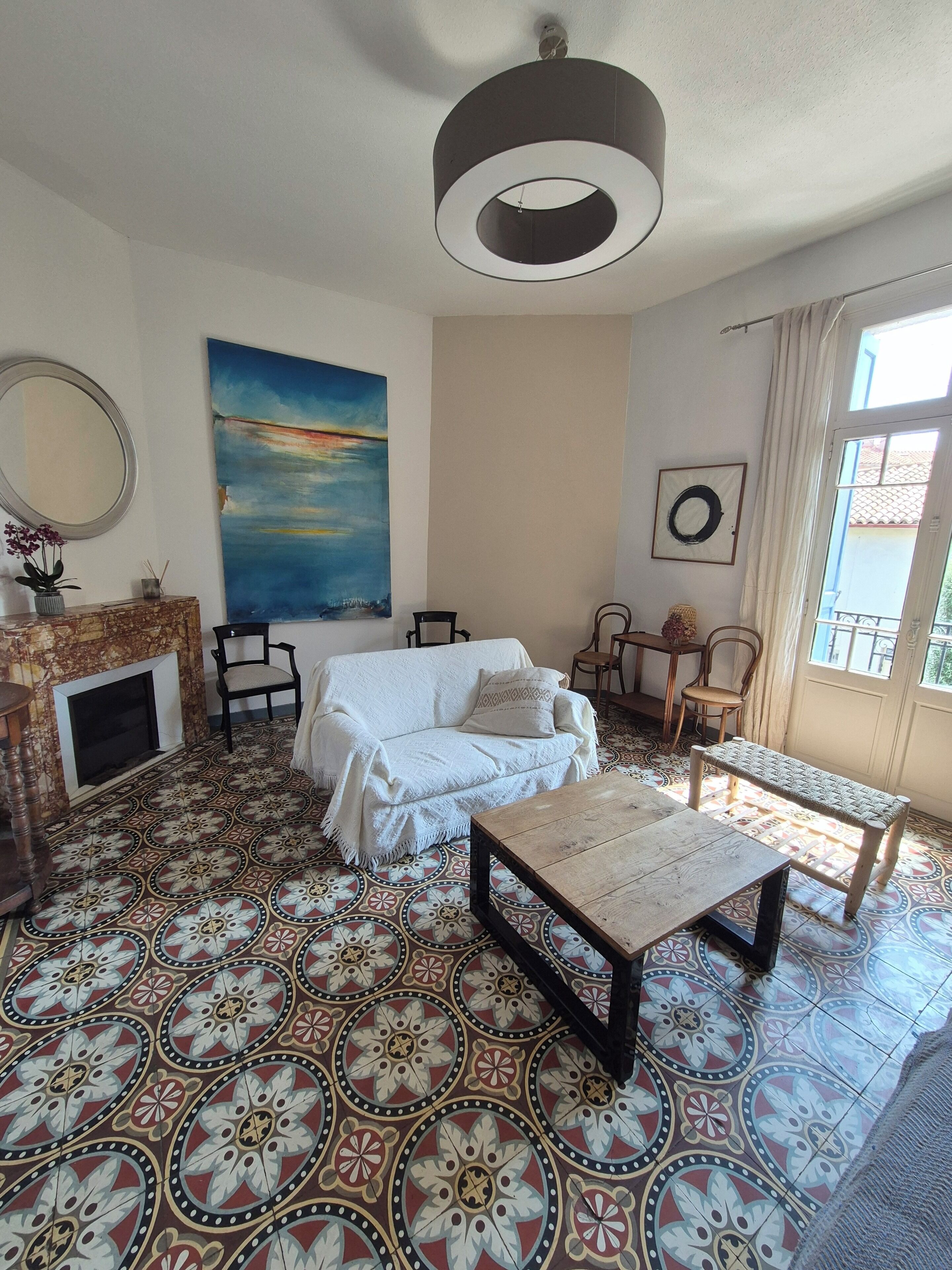 Un salon avec un sol à motifs, un canapé blanc, une table basse en bois et un grand tableau accroché au mur.