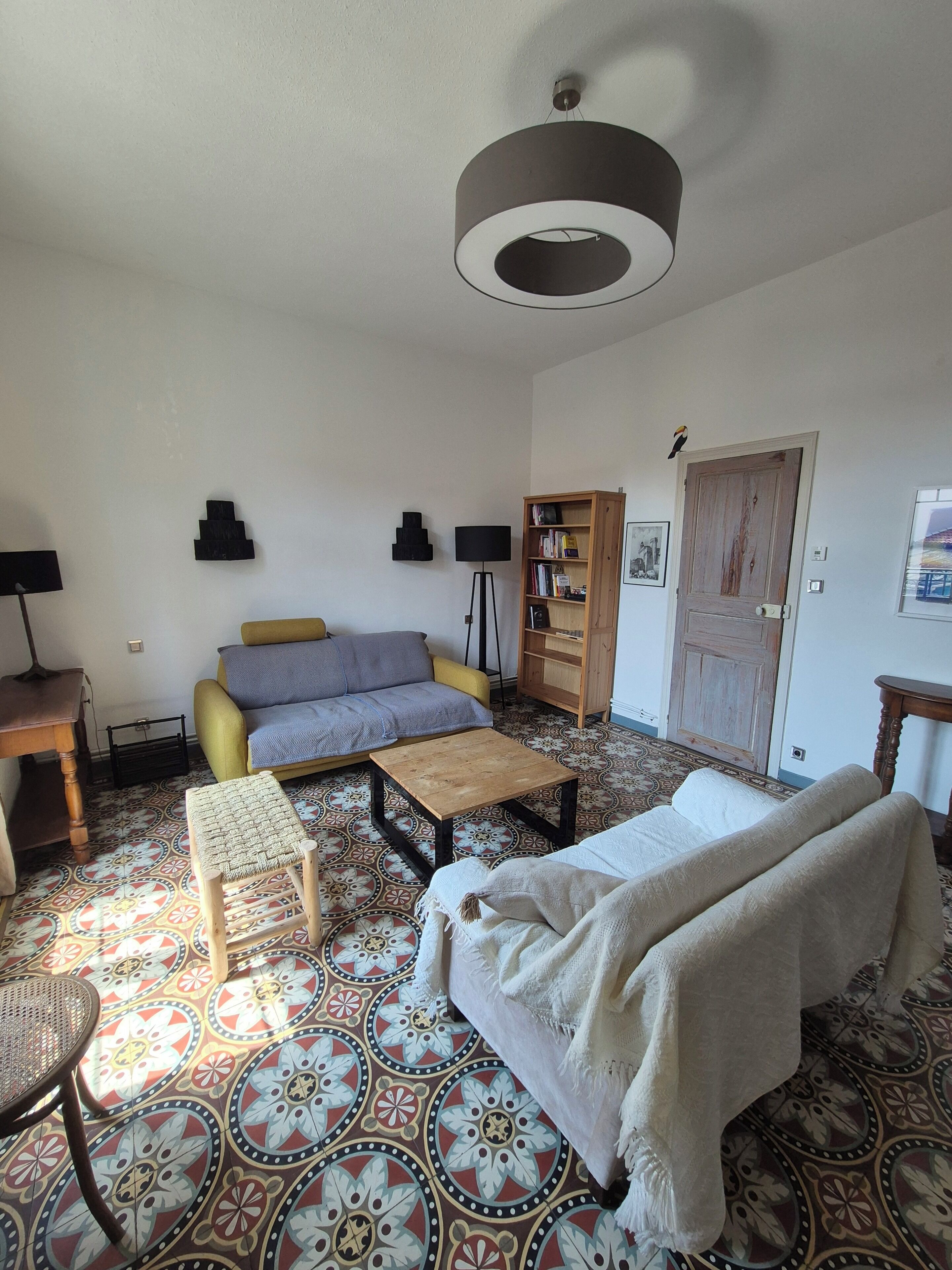Un salon comprenant un canapé, une table basse, un sol à motifs, une bibliothèque et une porte.