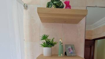 A bathroom with a toilet, a sink, a shower curtain, and two shelves with plants and a photo frame.
