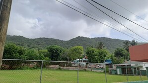 A fenced area with a view of a hill, a building with a blue roof, and a palm tree. - Fully furnished apartment in Los Patos, 5 minutes from the Rio de los Patos (Los Patos)