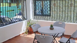 A patio with a round table and chairs, a potted plant, and a view of a swimming pool. - Fully furnished apartment in Los Patos, 5 minutes from the Rio de los Patos (Los Patos)