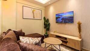 Un salón con un sofá marrón, una mesa de centro, un televisor montado en la pared y una planta en maceta.