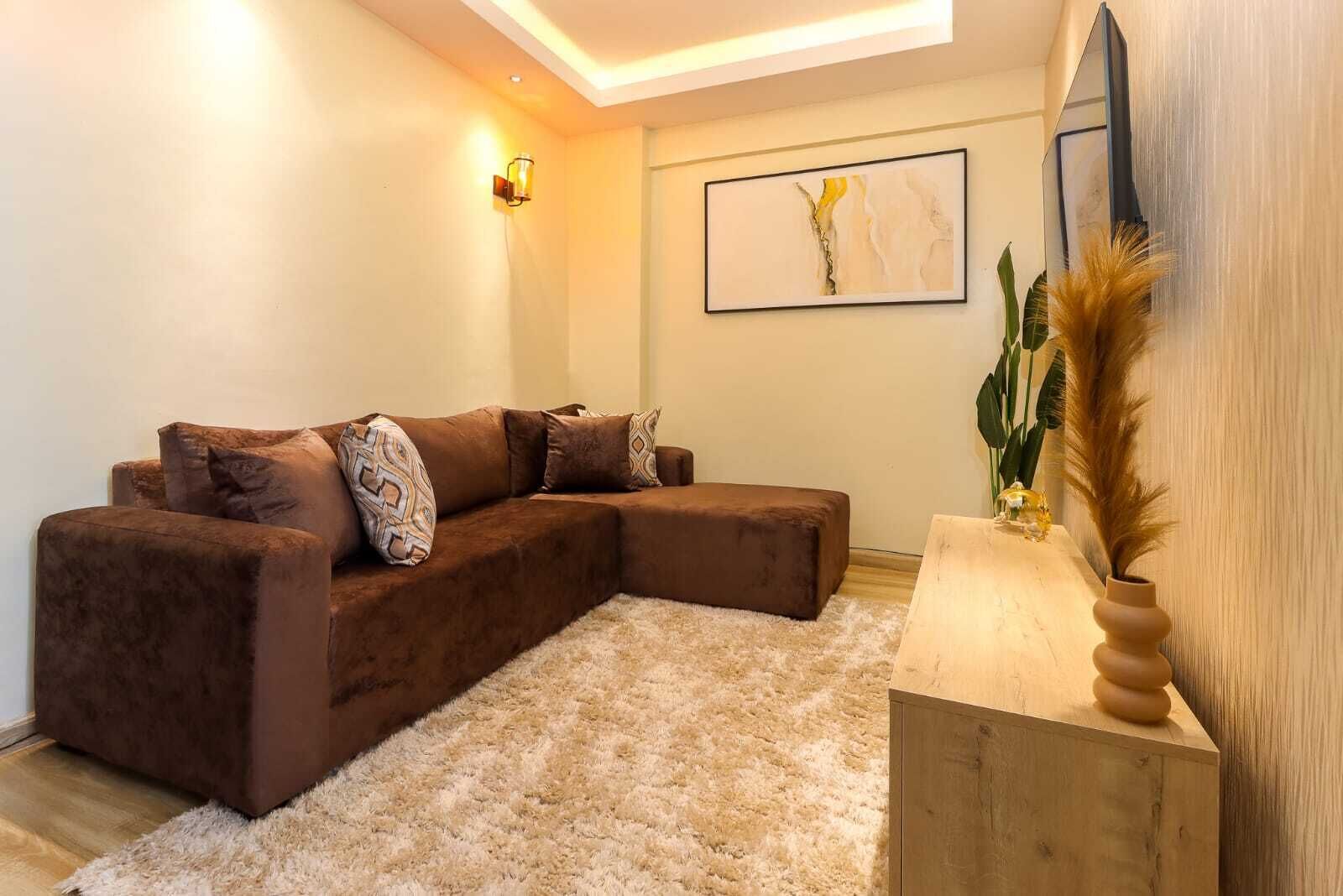 A modern living room with a brown sectional sofa, a fluffy rug, and a wooden side table with a vase.