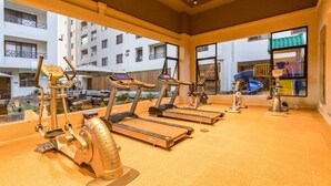 Un gimnasio con cintas de correr, elípticas y una bicicleta estática, con vistas a una zona residencial a través de amplios ventanales.
