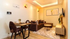 Una sala de estar moderna con un sofá marrón, una mesa de comedor con sillas, una mesita redonda y un tapete de colores claros.