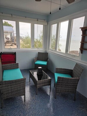 A room with wicker furniture, a glass coffee table, and large windows overlooking a body of water. - Oak Harbor Lake Erie Beach Front Cabin 3Bed 1Bath (Oak Harbor)