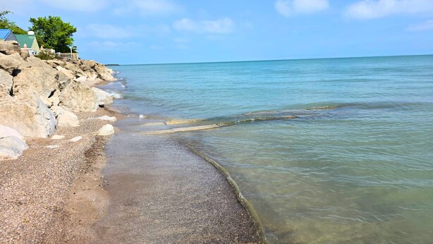 A beach with clear water, a rocky shoreline, and a house with a green roof. - Oak Harbor Lake Erie Beach Front Cabin 3Bed 1Bath (Oak Harbor)
