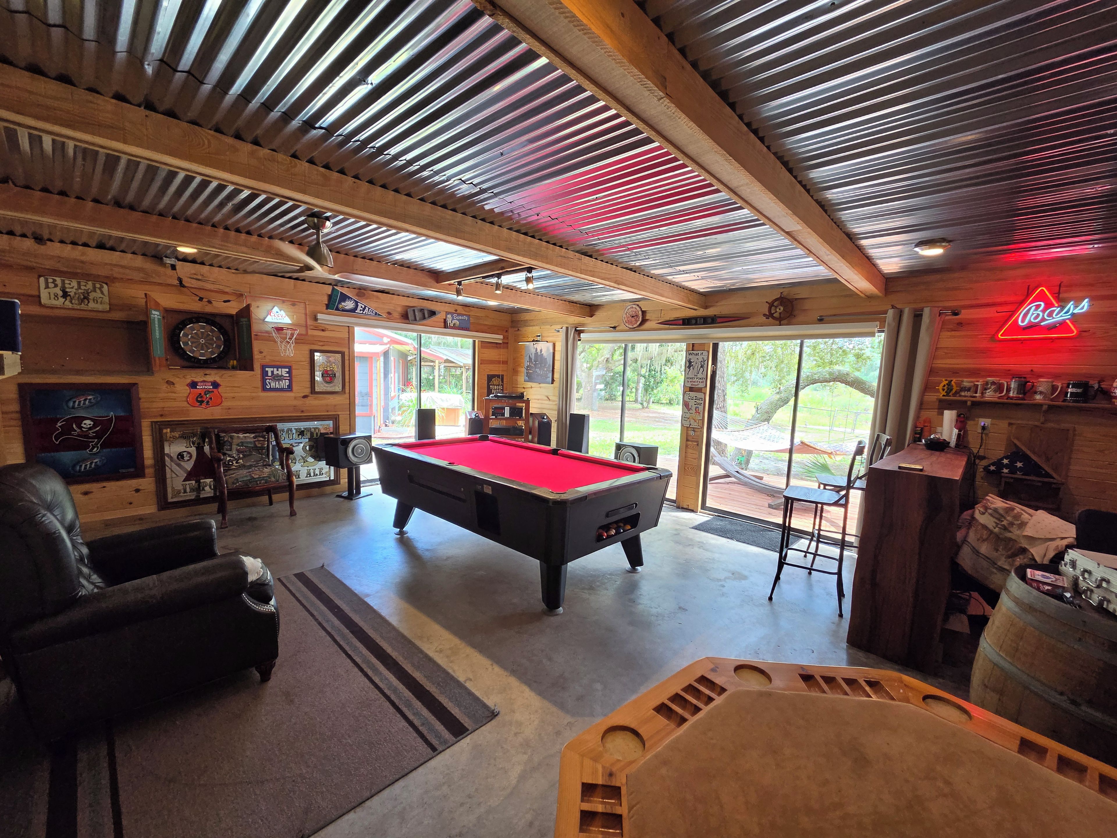 A pool table in a room with wooden walls, a neon sign, and a view of the outdoors.