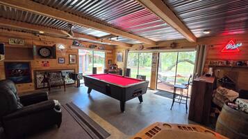 A pool table in a room with wooden walls, a neon sign, and a view of the outdoors.