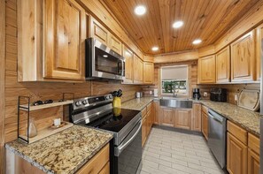 A kitchen with wooden cabinets, stainless steel appliances, granite countertops, and a window with a view.