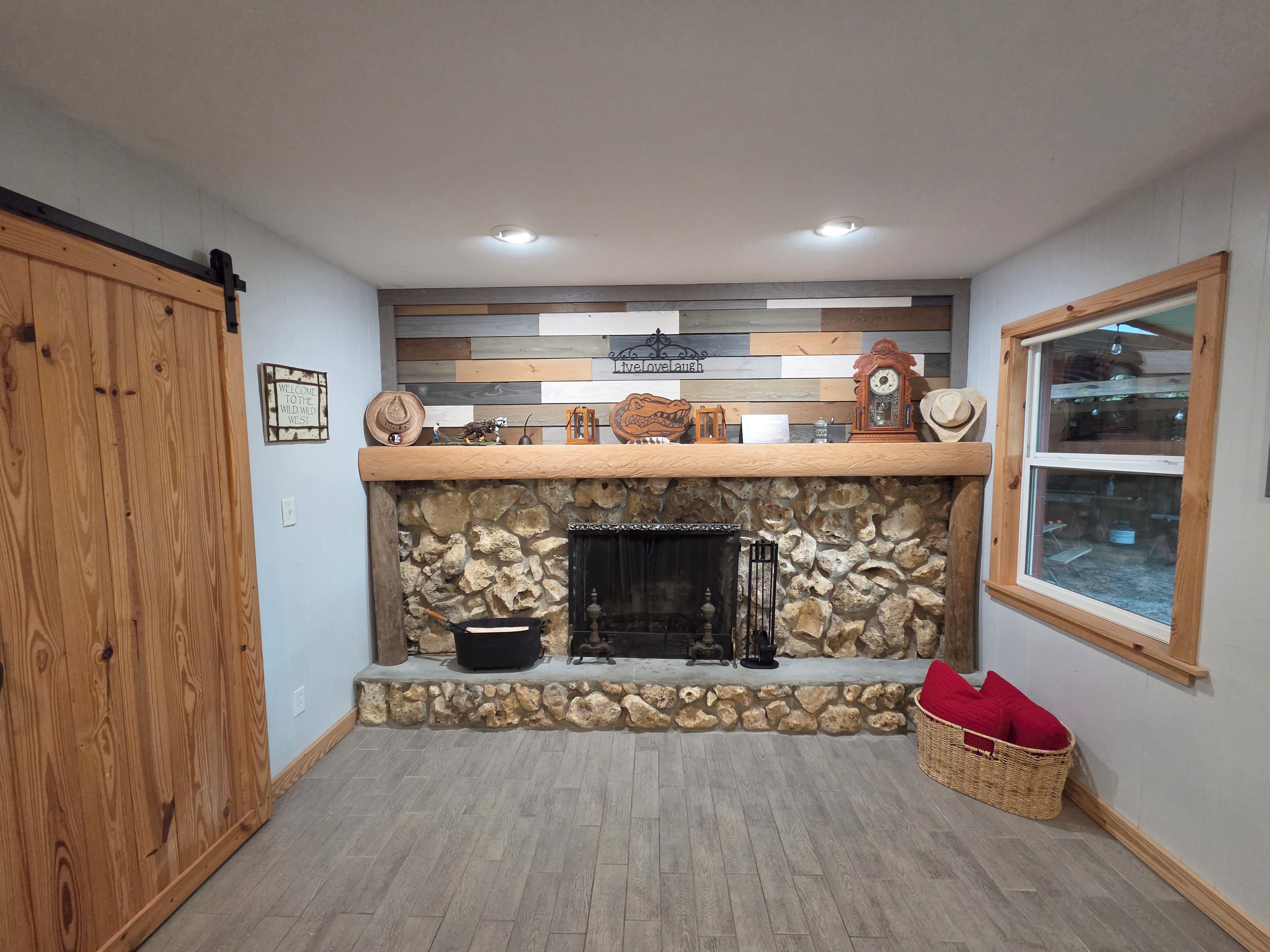 A room with a stone fireplace, wooden walls, and a window.