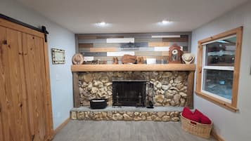 A room with a stone fireplace, wooden walls, and a window.