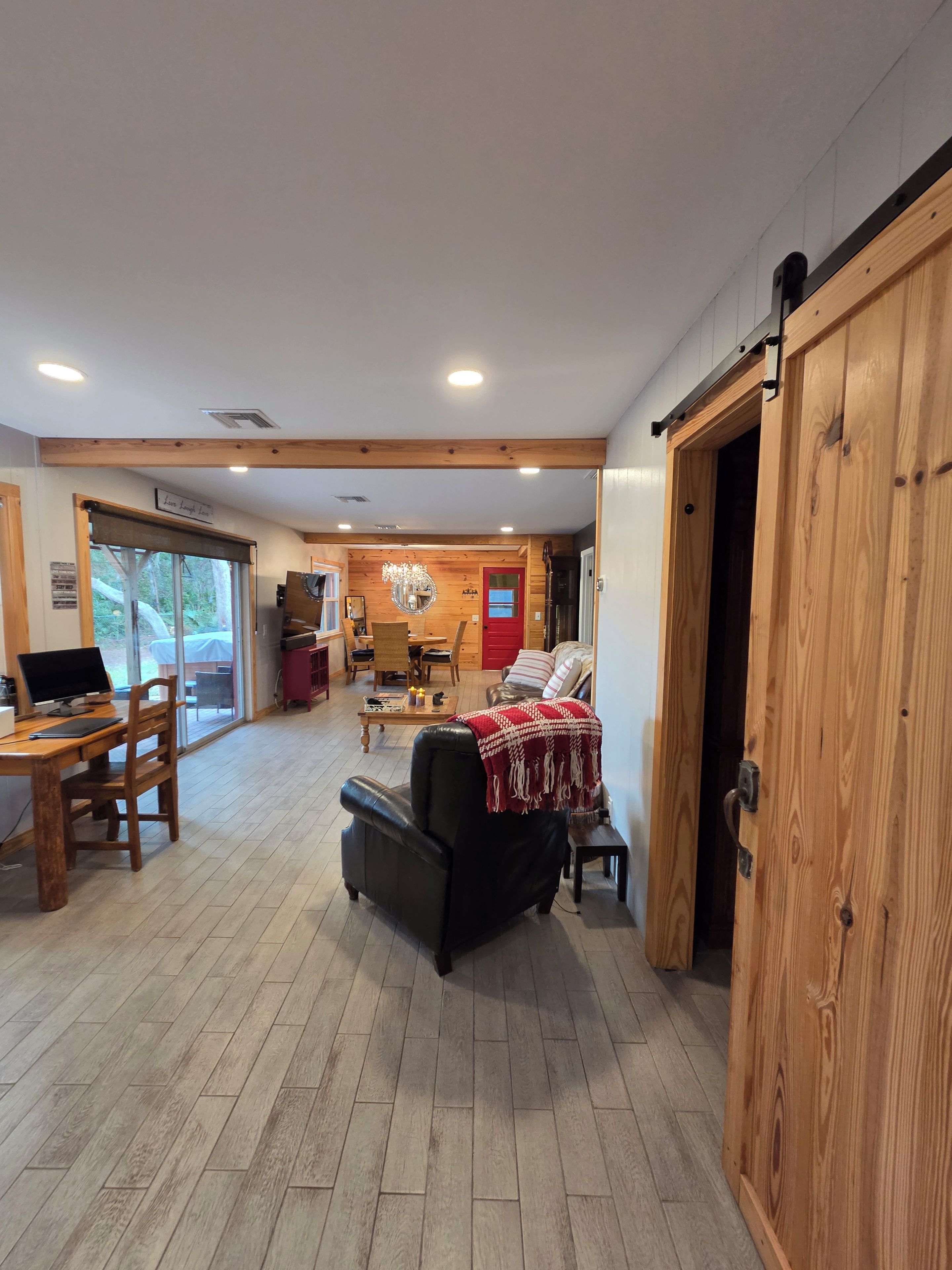 A spacious living area with a wooden floor, a leather sofa, a dining table with chairs, and a kitchen in the background.