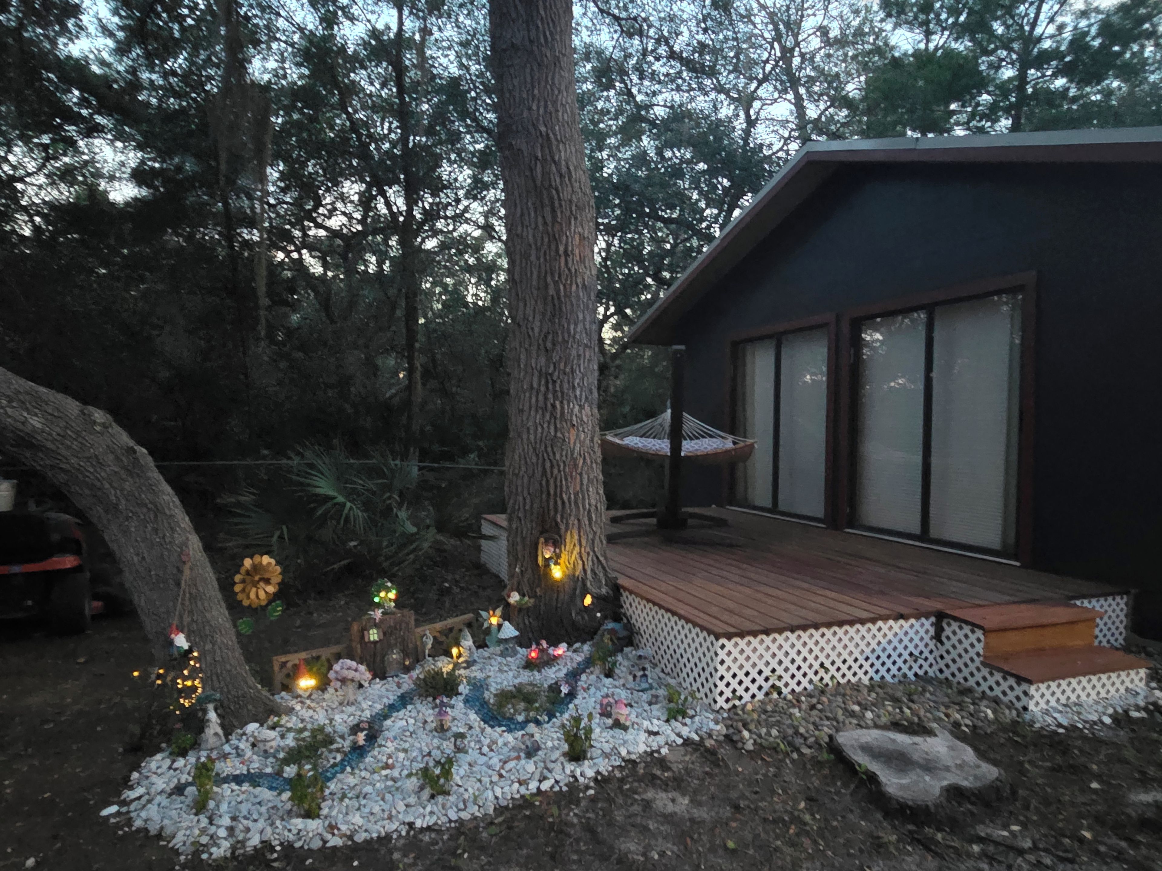 A modern house with a deck, surrounded by trees and a garden with decorative lights.