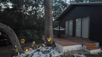 A modern house with a deck, surrounded by trees and a garden with decorative lights.